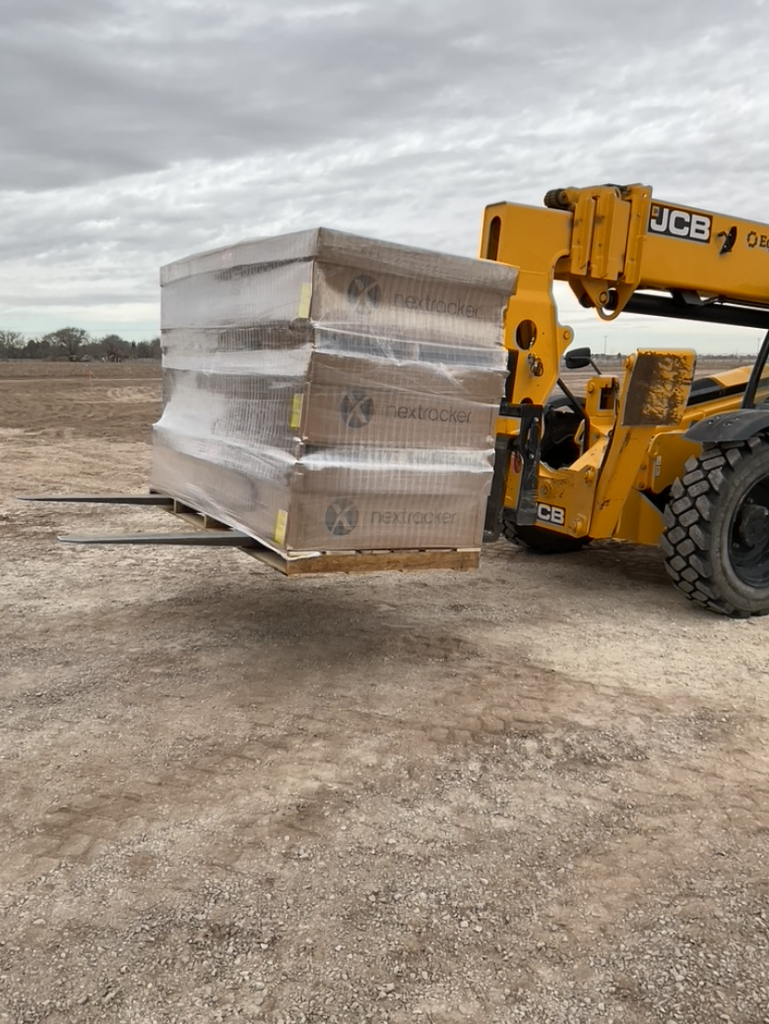 Telehandler transporting pre-kitted project boxes at a solar project site, prepared for delivery to their designated installation locations.